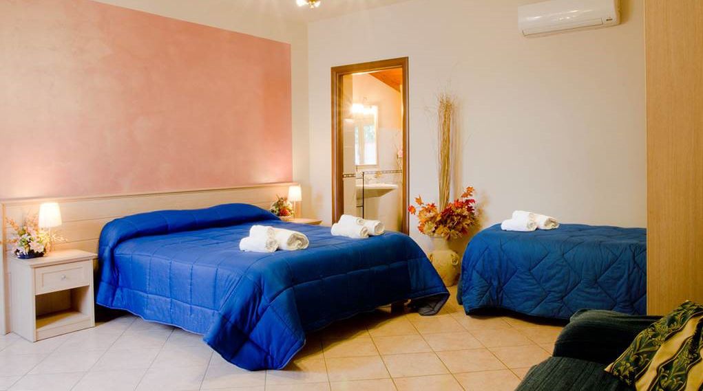 A hotel room with two beds, a nightstand, a mirror, and a vase with flowers.