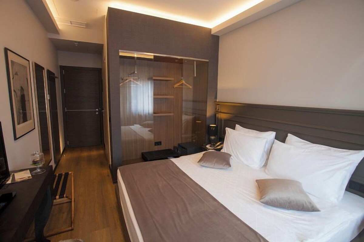 A hotel room with a bed, bedside table, lamp, and a wardrobe with a mirror.