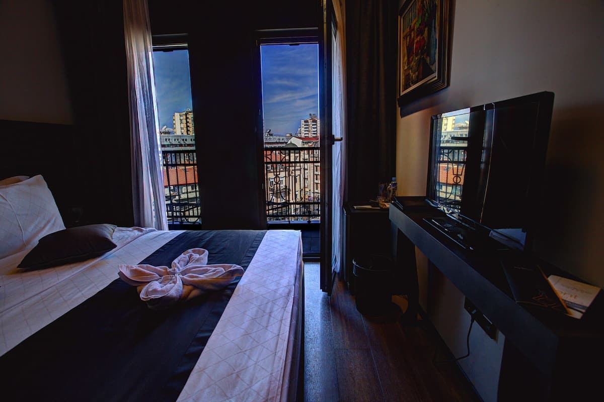 Ein Hotelzimmer mit Bett, Fernseher, Schreibtisch und Blick auf Gebäude durch das Fenster.
