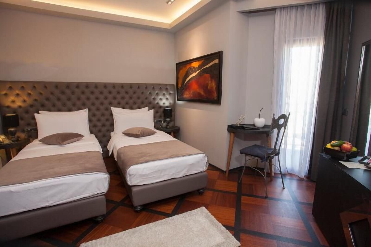 A hotel room with two beds, a desk, a chair, and a painting on the wall.