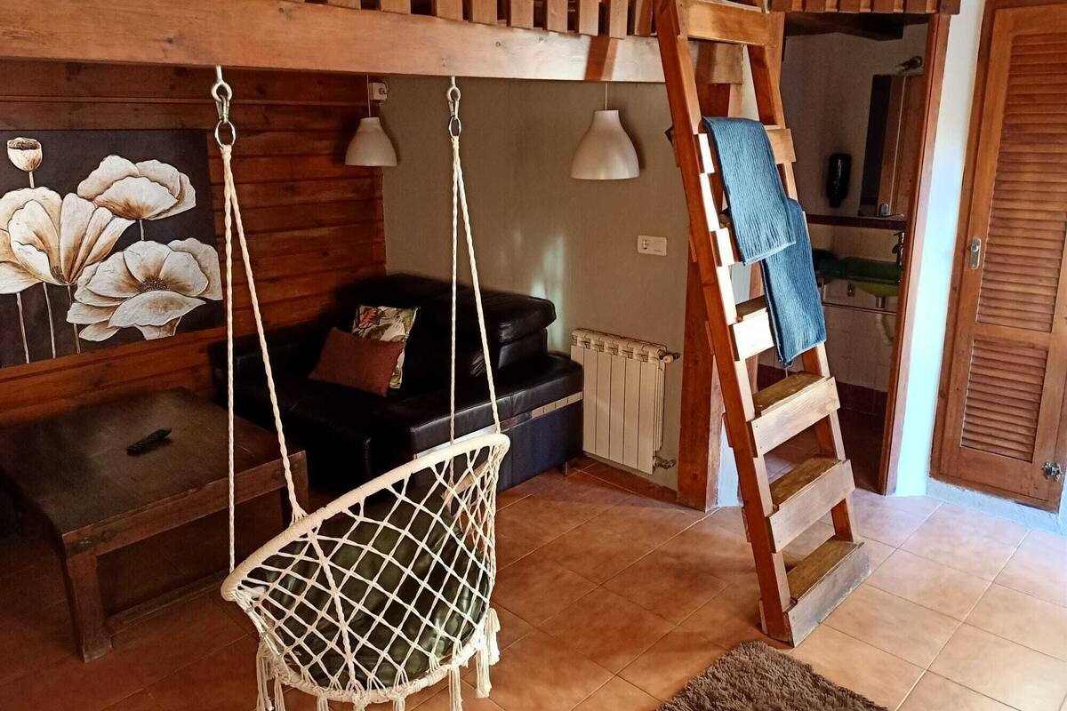 Ein Zimmer mit einer Hängematten-Stuhlschaukel, einer Holzleiter, einem schwarzen Sofa und einer Wandleuchte.