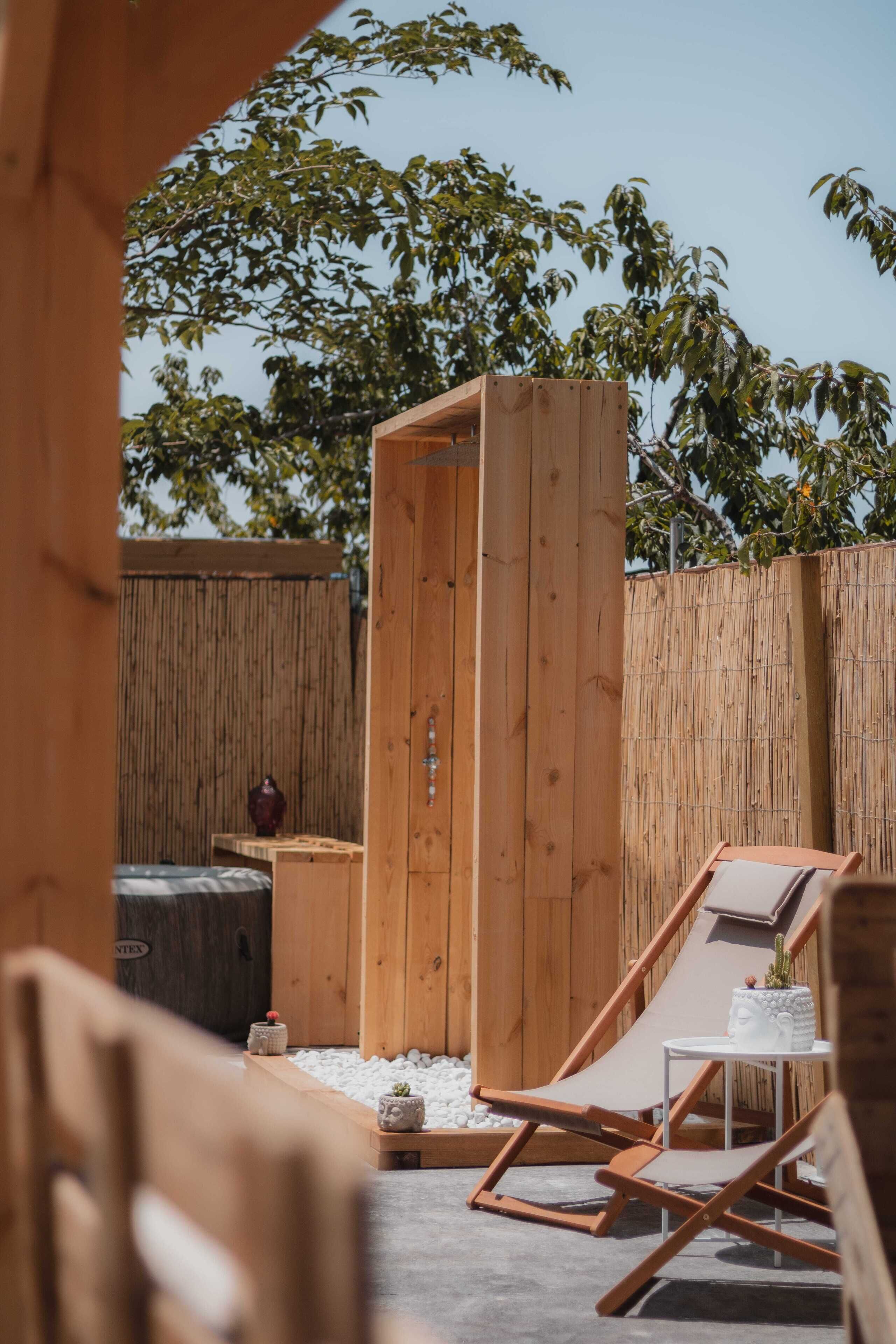 Un área de estar exterior de madera con un jacuzzi, una estructura de madera y una valla de bambú.