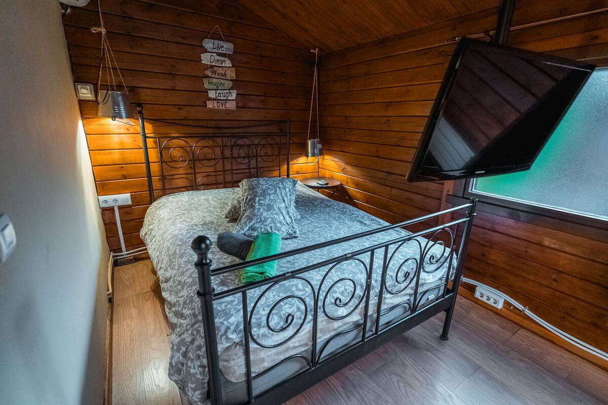 Ein gemütliches Schlafzimmer mit einem Metallbettgestell, einer Holzzahlendele und einem an der Wand montierten Fernseher.