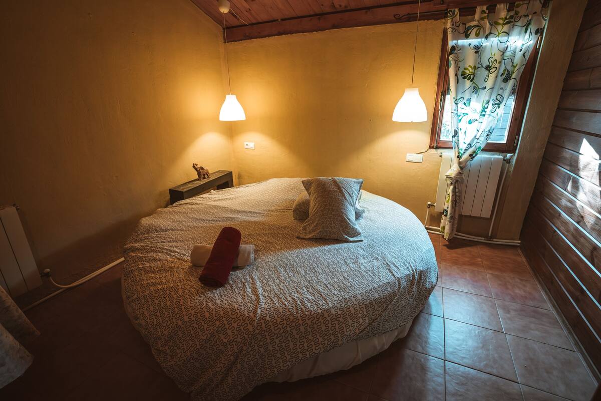 Ein gemütliches Schlafzimmer mit einem großen Bett, zwei Nachttischlampen, einem Nachttisch und einem Fenster mit Vorhängen.