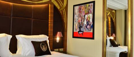 Habitación de hotel con una cama grande, cabecero con diseño decorativo, un cuadro en la pared y un espejo que refleja la habitación.