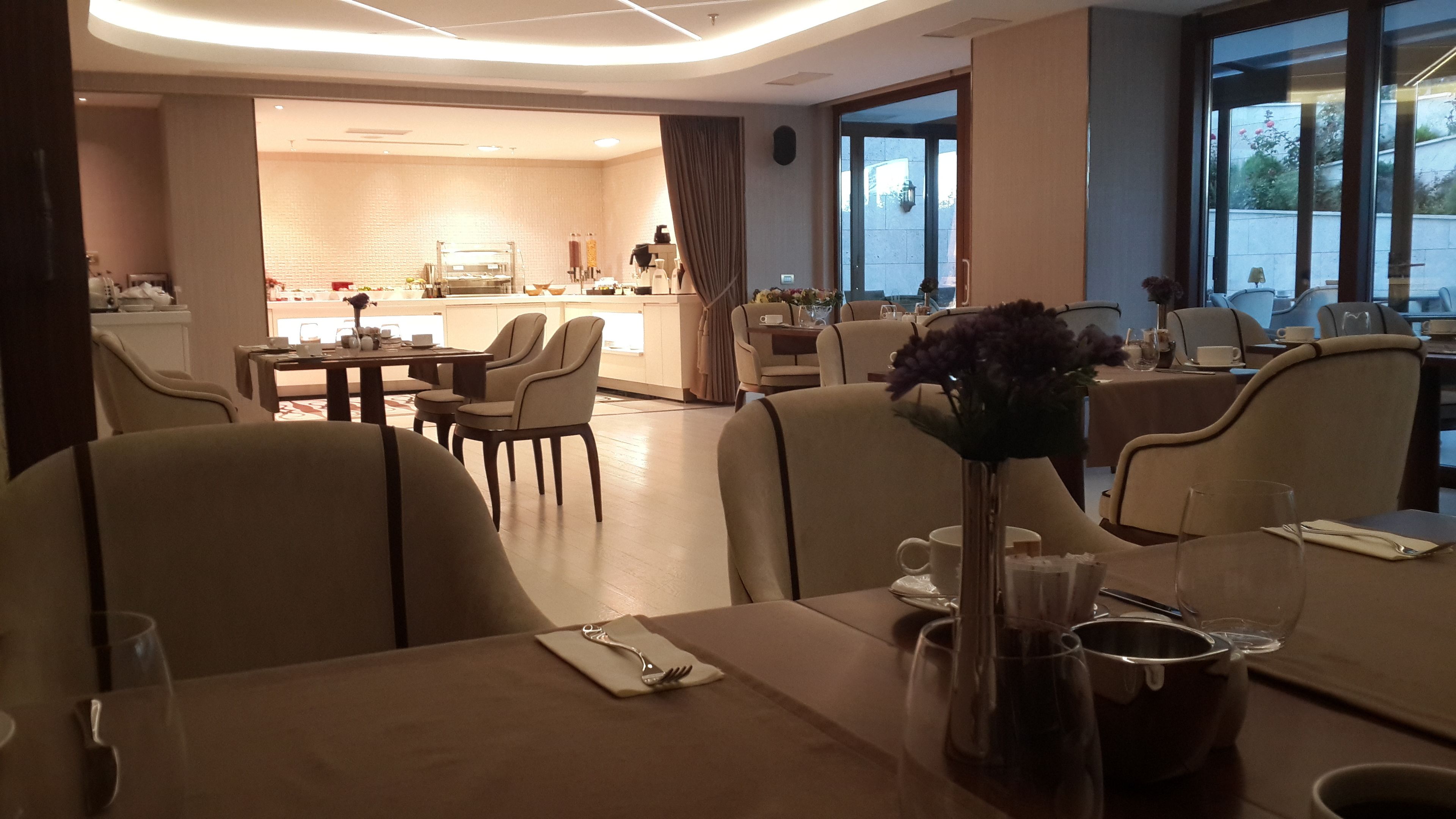 A dining area with tables set for two, chairs, and a vase with flowers.