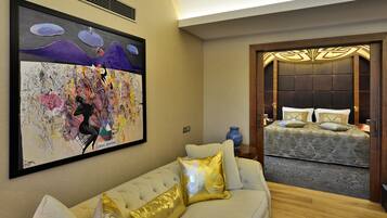 A hotel room with a large abstract painting on the wall, a tufted sofa with gold pillows, and a bed with patterned bedding.