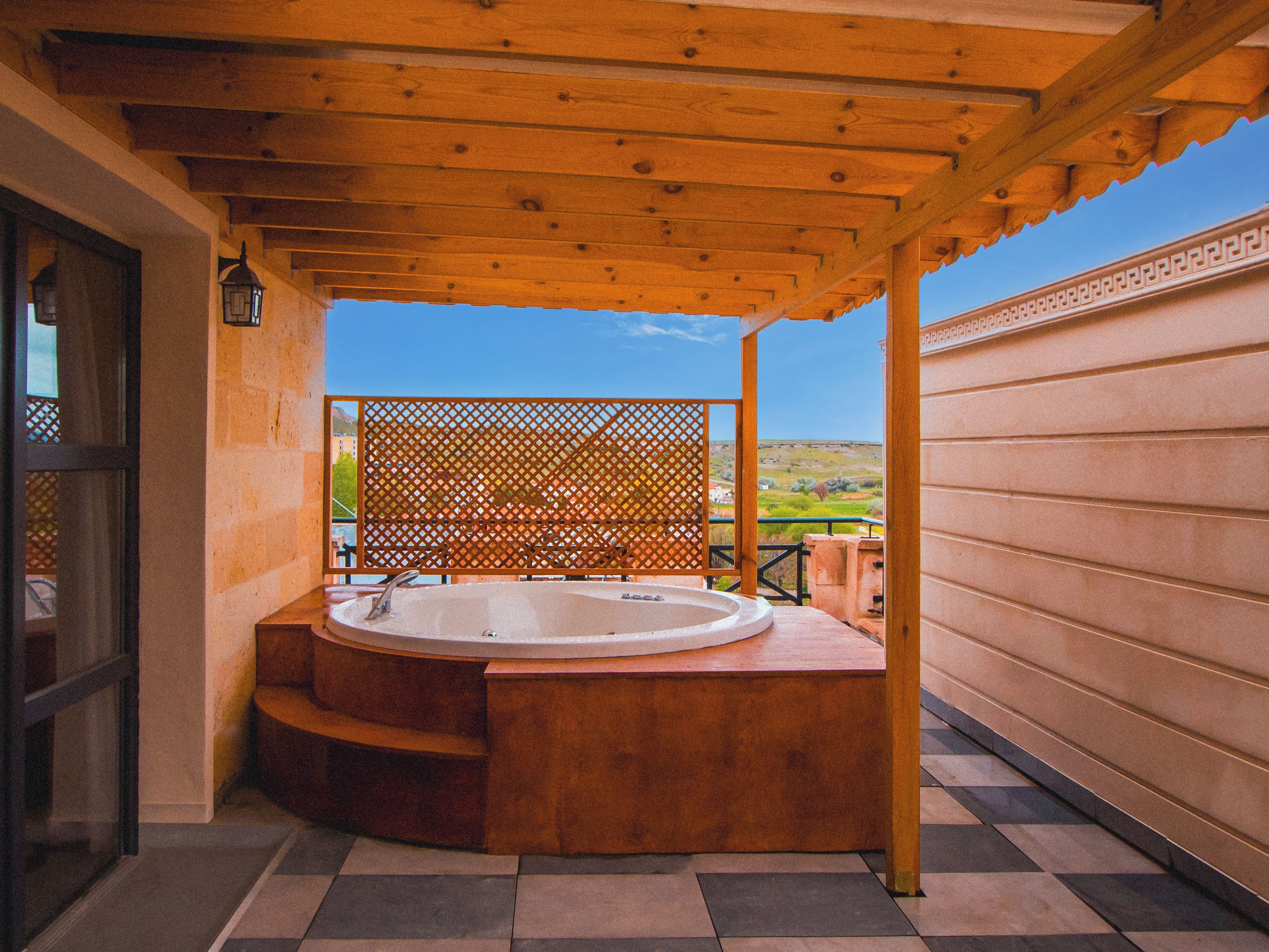 A hot tub under a wooden pergola with a view of a green landscape.
