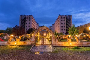 A gated entrance with a stone archway leading to a building with multiple floors and a fire escape on each side.