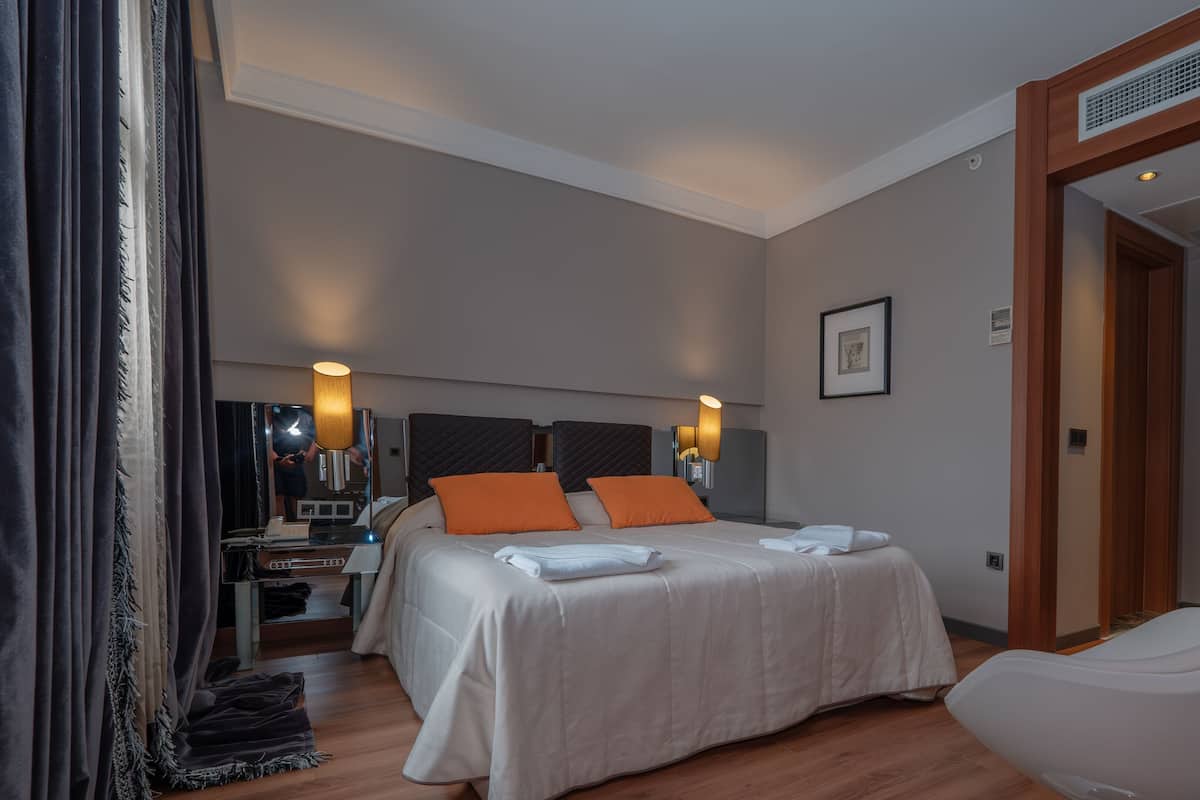 A hotel room with a large bed, two bedside lamps, a desk with a chair, a mirror, and a door to the bathroom.