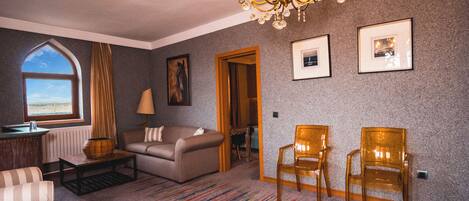 A room with a large window, a chandelier, a sofa, two chairs, and a carpeted floor.