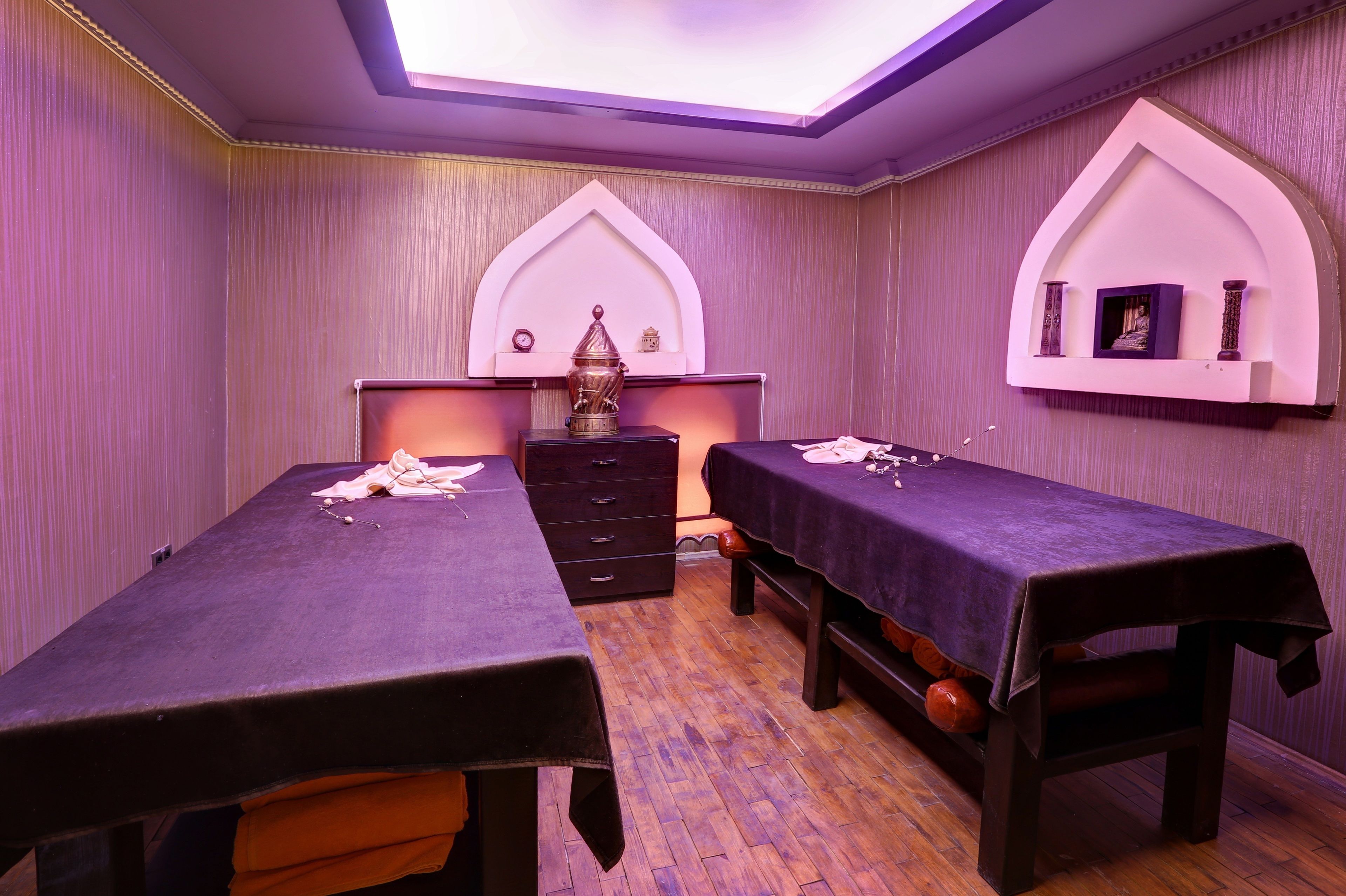 A room with two beds, a chest of drawers, and a small table with a lamp.