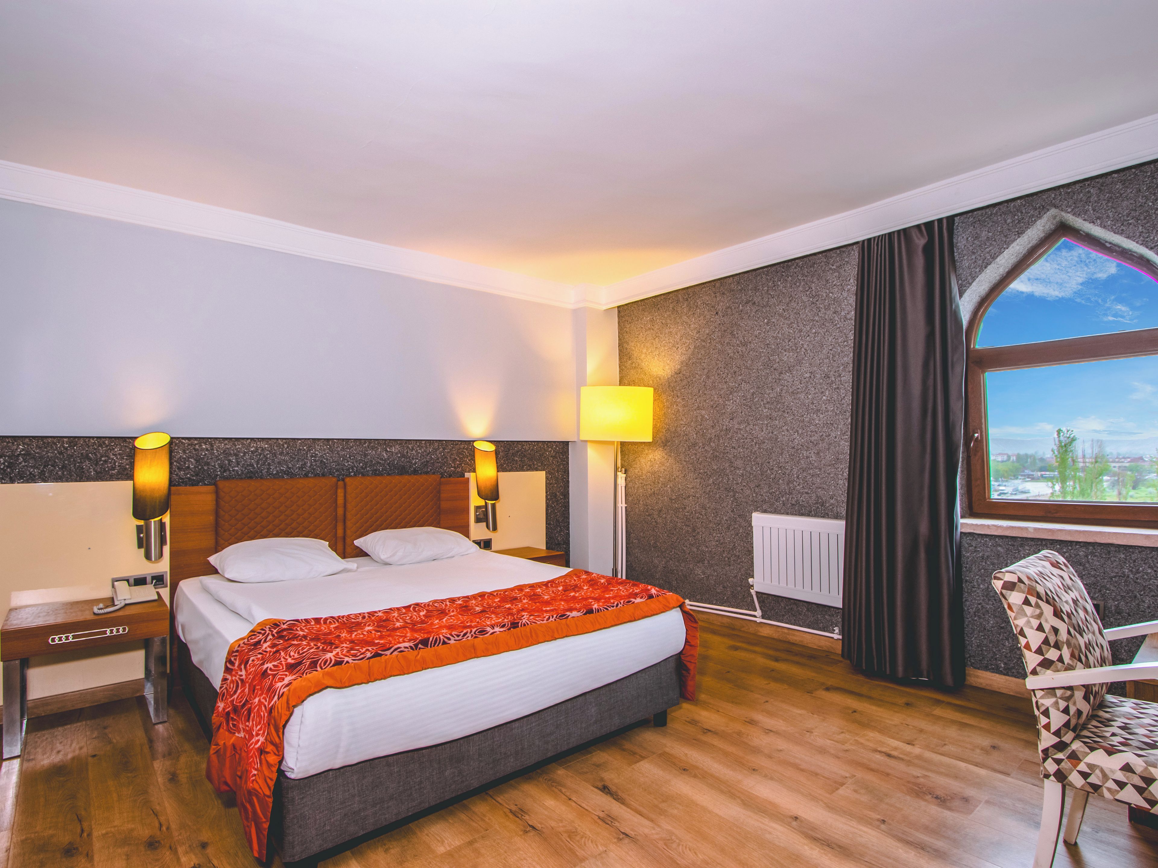 Quarto de hotel com cama, mesas de cabeceira, uma cadeira, janela com vista e luminária.