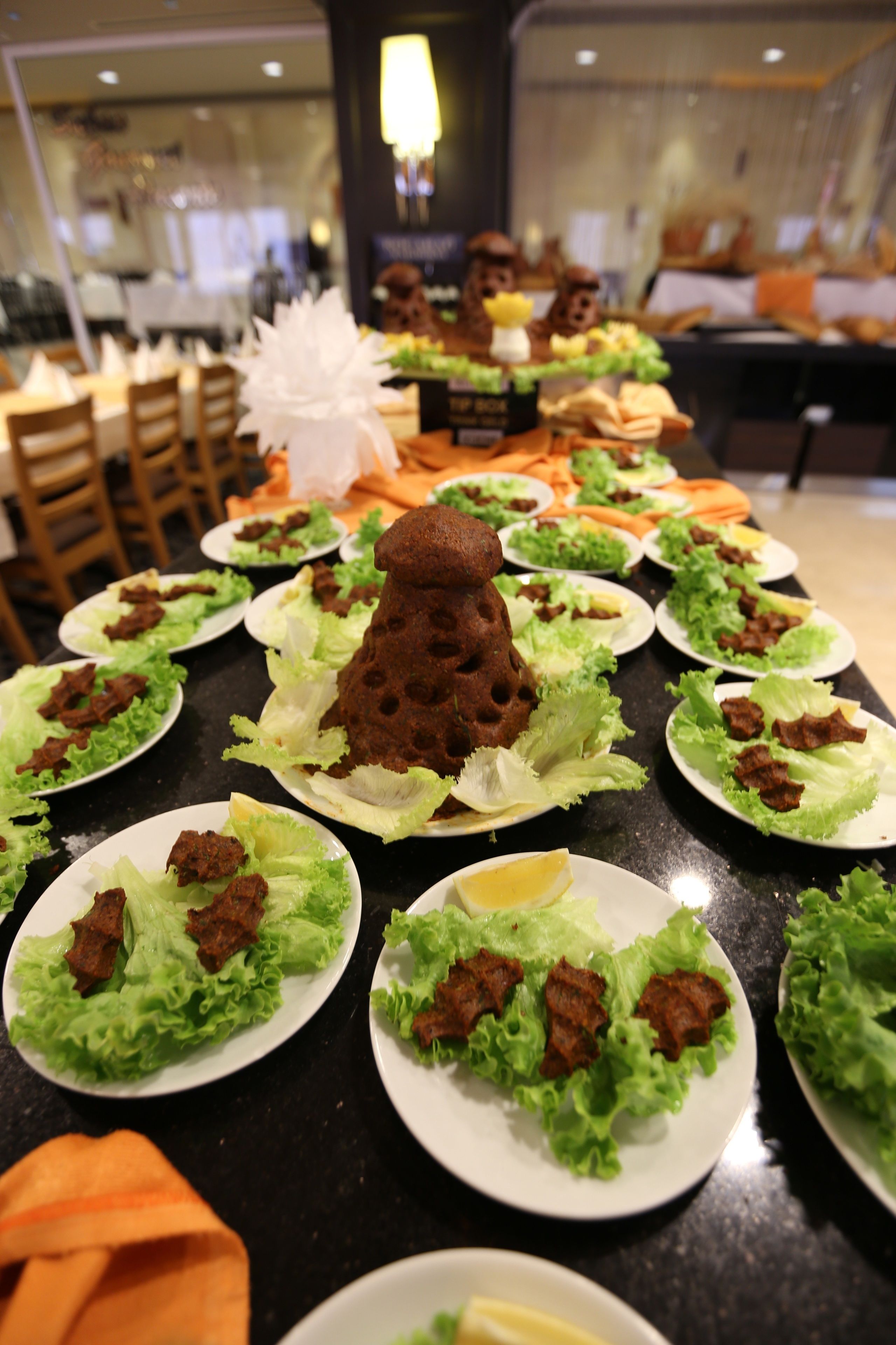 En buffet med tallerkener med mad, herunder salat og kød, samt en dekorativ midtpunkt.