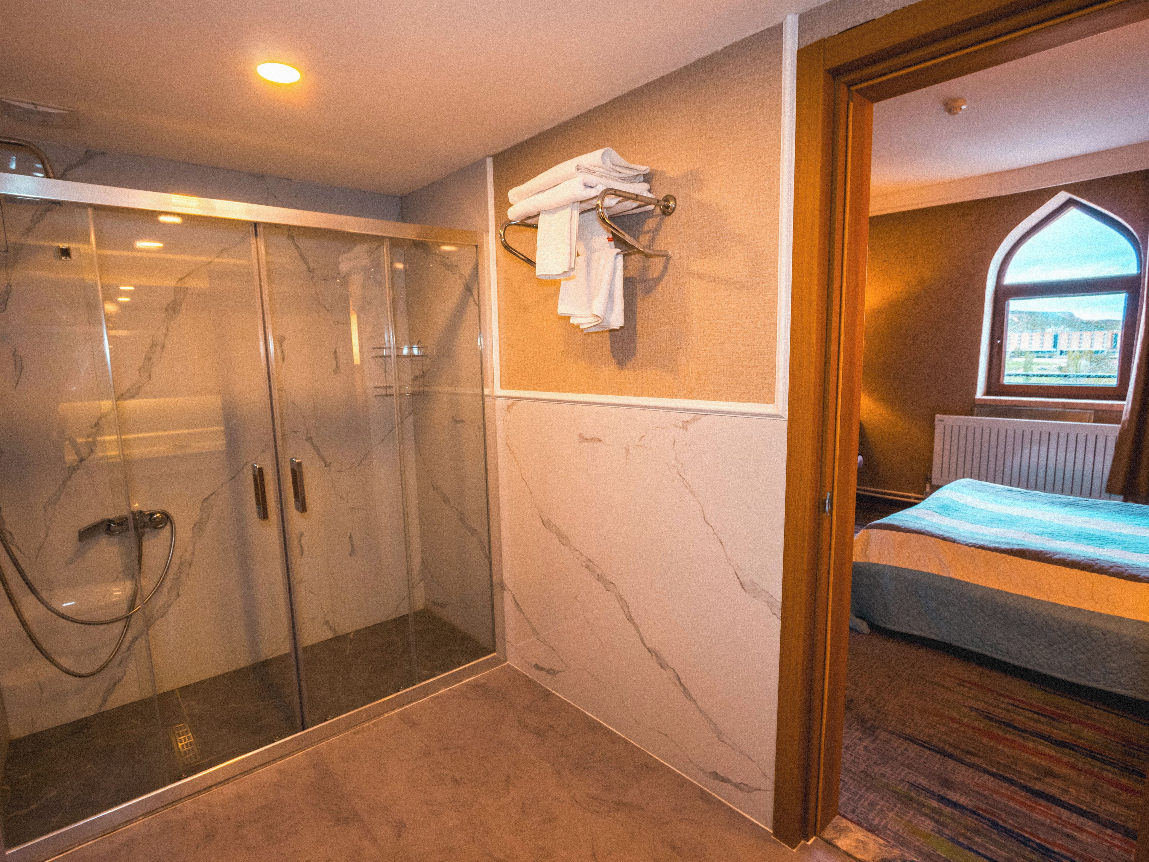 Une salle de bain d’hôtel avec une douche en verre, un lit avec vue et un porte-serviettes.