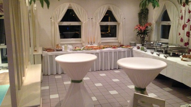 A banquet hall with a long table set for a meal, two round tables with white coverings, and a window with a view of the night sky.