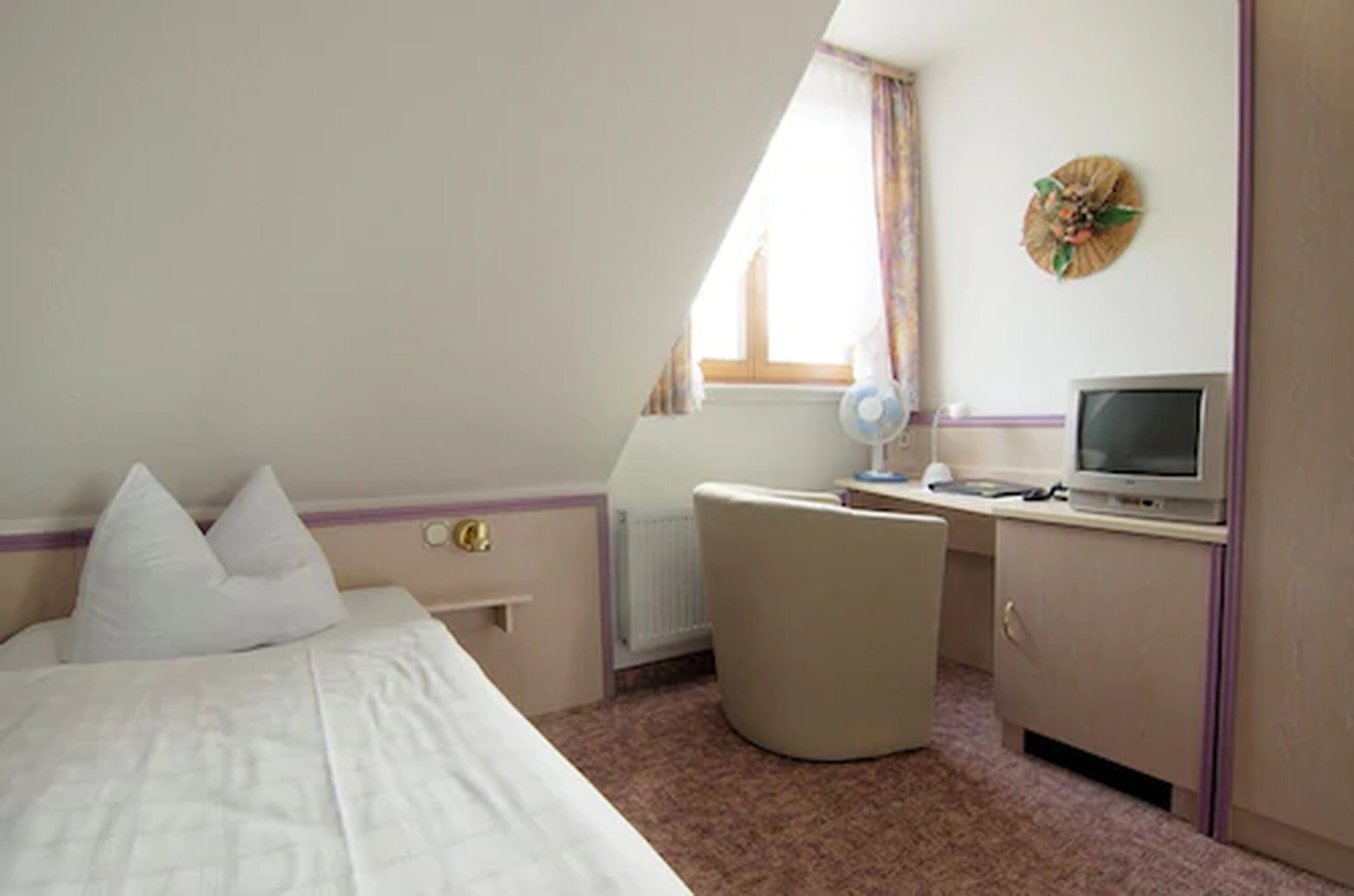 A hotel room with a bed, a desk with a computer, a chair, and a window with curtains.