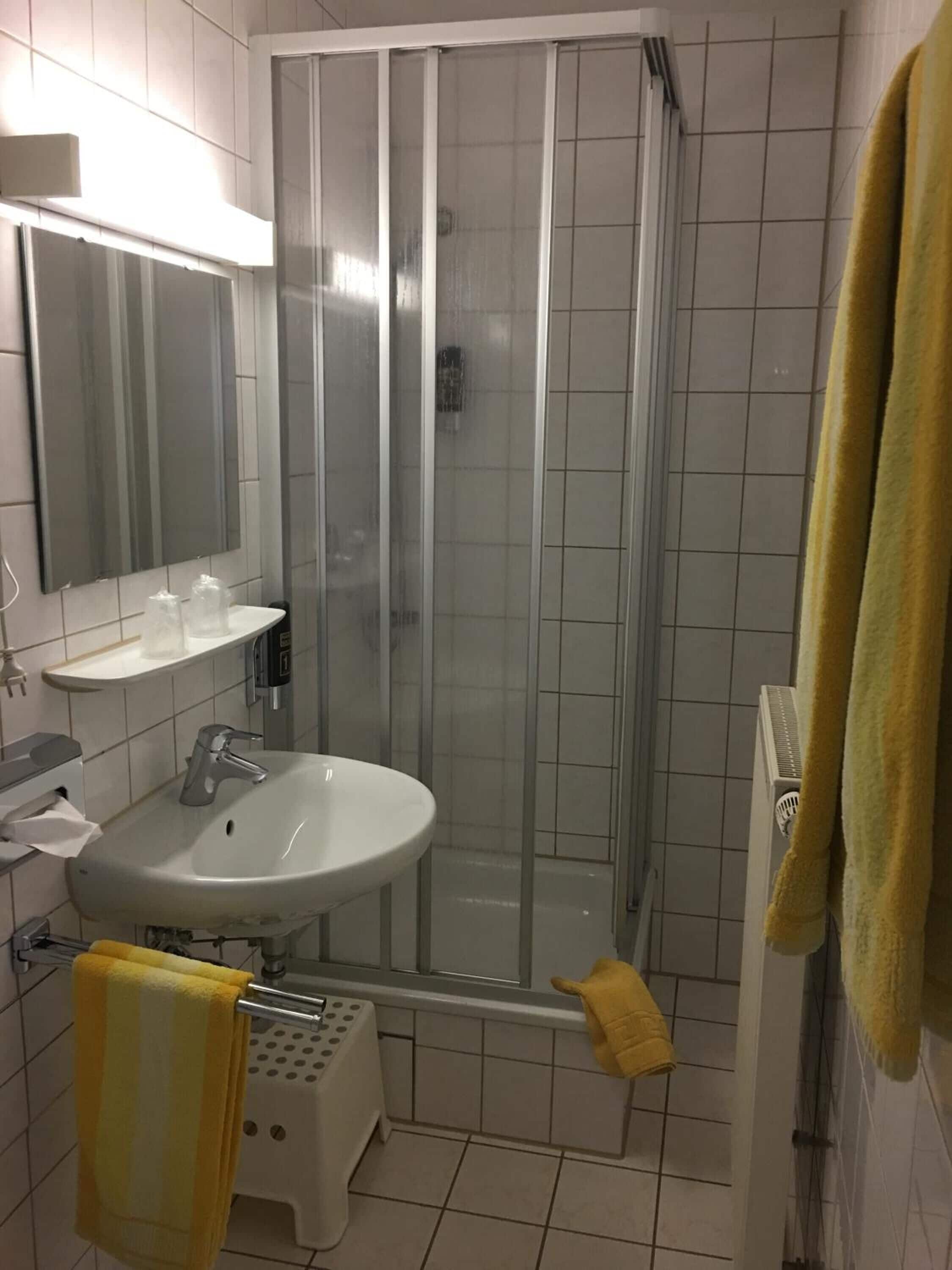 A bathroom with a glass-enclosed shower, a sink with a mirror above it, and a towel rack with a yellow towel.