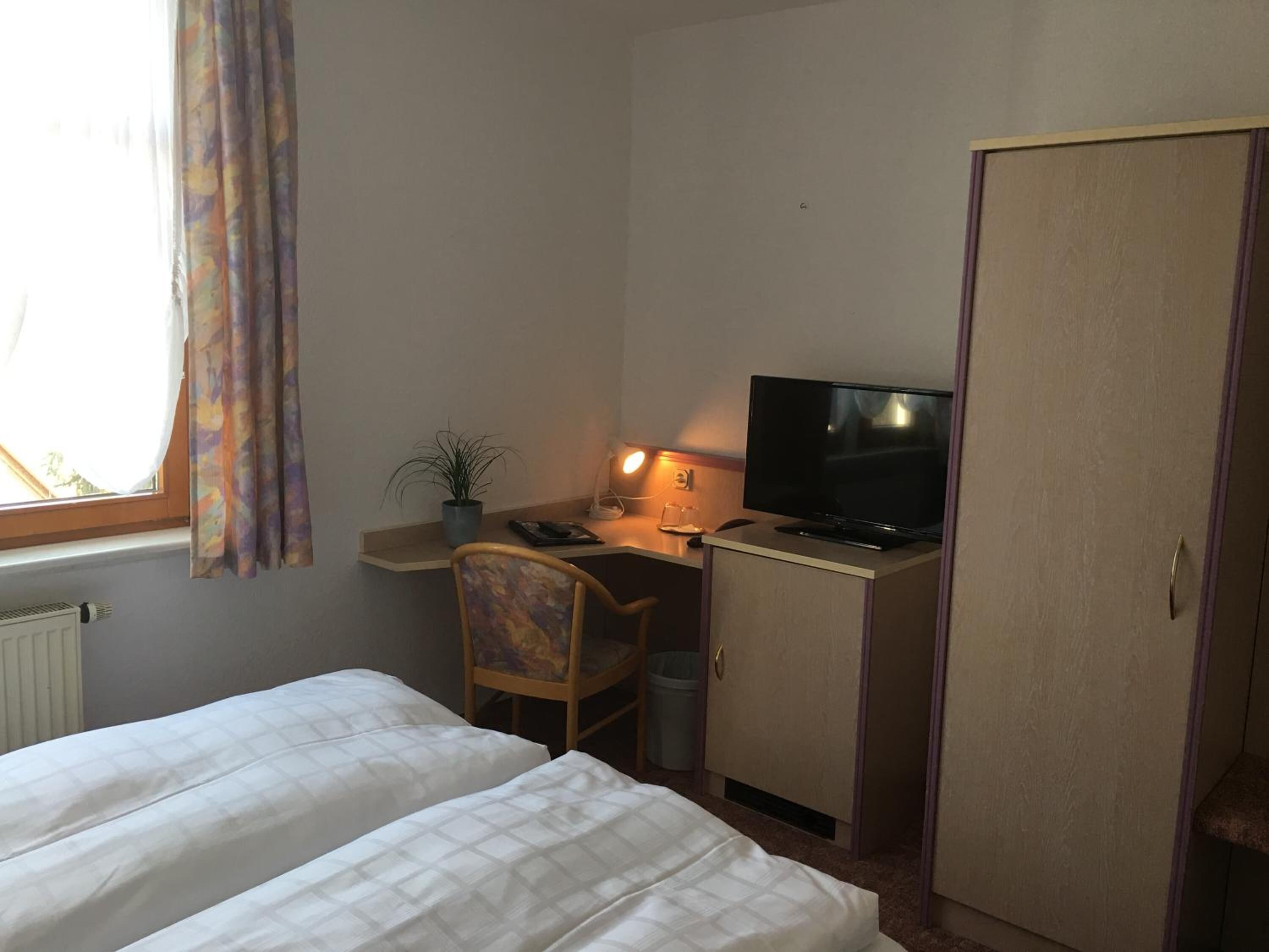 A room with two beds, a desk with a computer and TV, a chair, a potted plant, and a wardrobe.