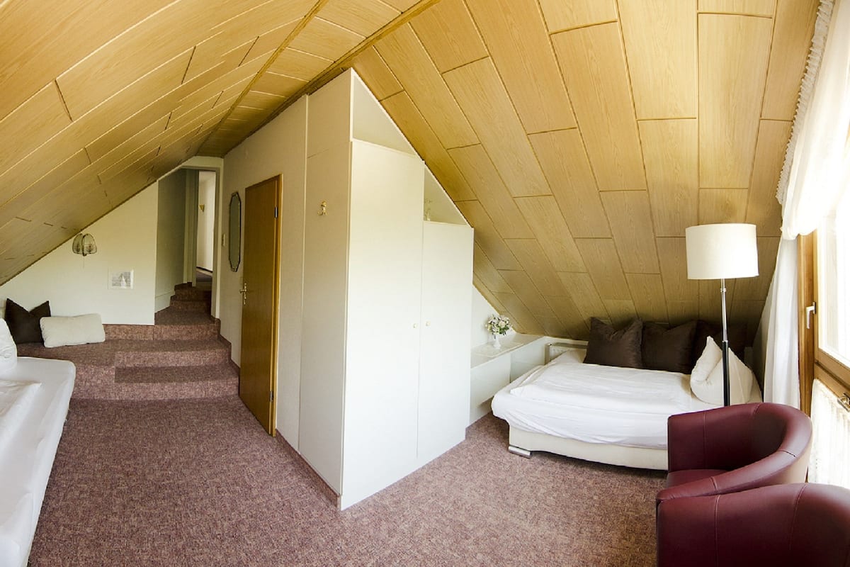 Une chambre avec un plafond en pente, un lit, une chaise et un escalier menant à une autre pièce.