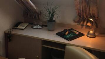 Una habitación pequeña con un tragaluz, un escritorio con una planta, una lámpara y una silla.