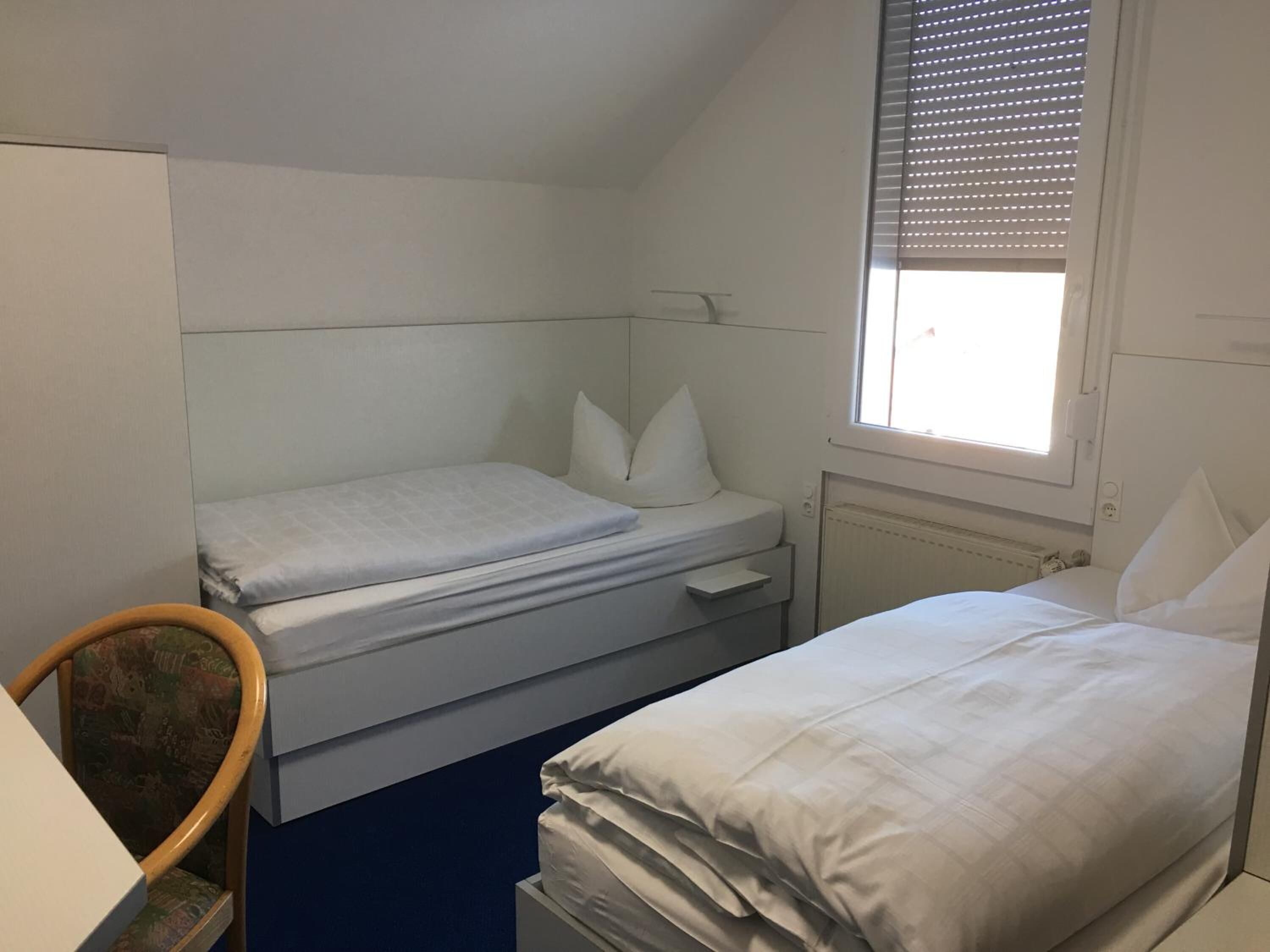 A small, single-bed room with a window, a desk, and a chair.