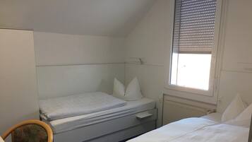 A small, single-bed room with a window, a desk, and a chair.