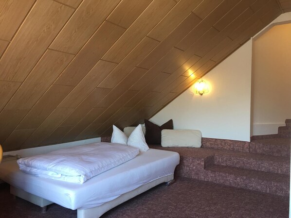 A bedroom with a sloped ceiling, a bed with white bedding, a nightstand, and a wall-mounted light fixture.