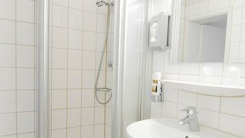Un baño con ducha de vidrio, un lavabo blanco y un espejo sobre el lavabo.