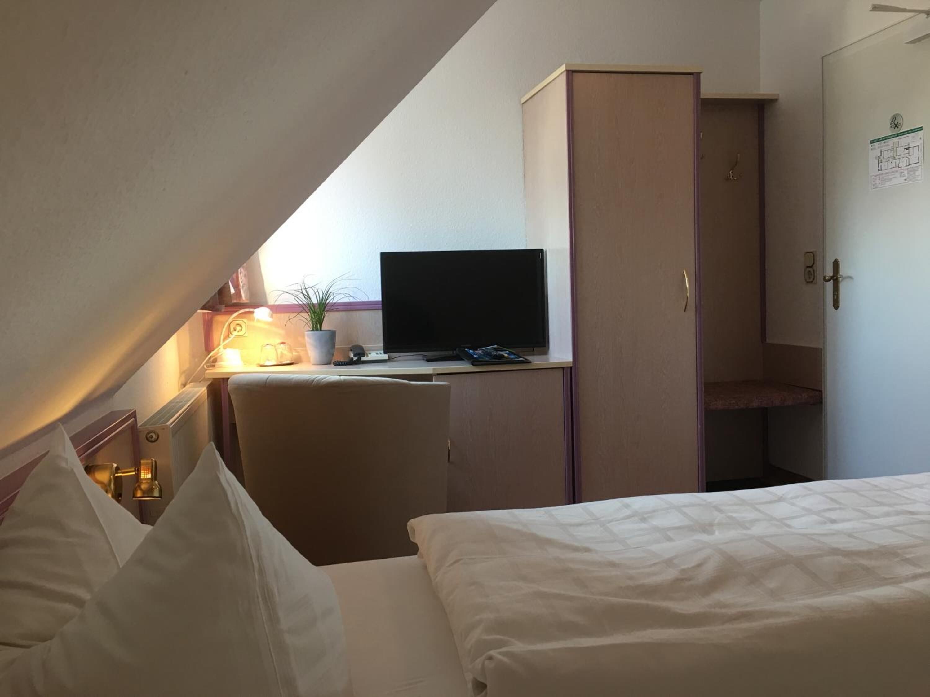 A small, compact room with a bed, a desk with a computer, a chair, and a wardrobe.