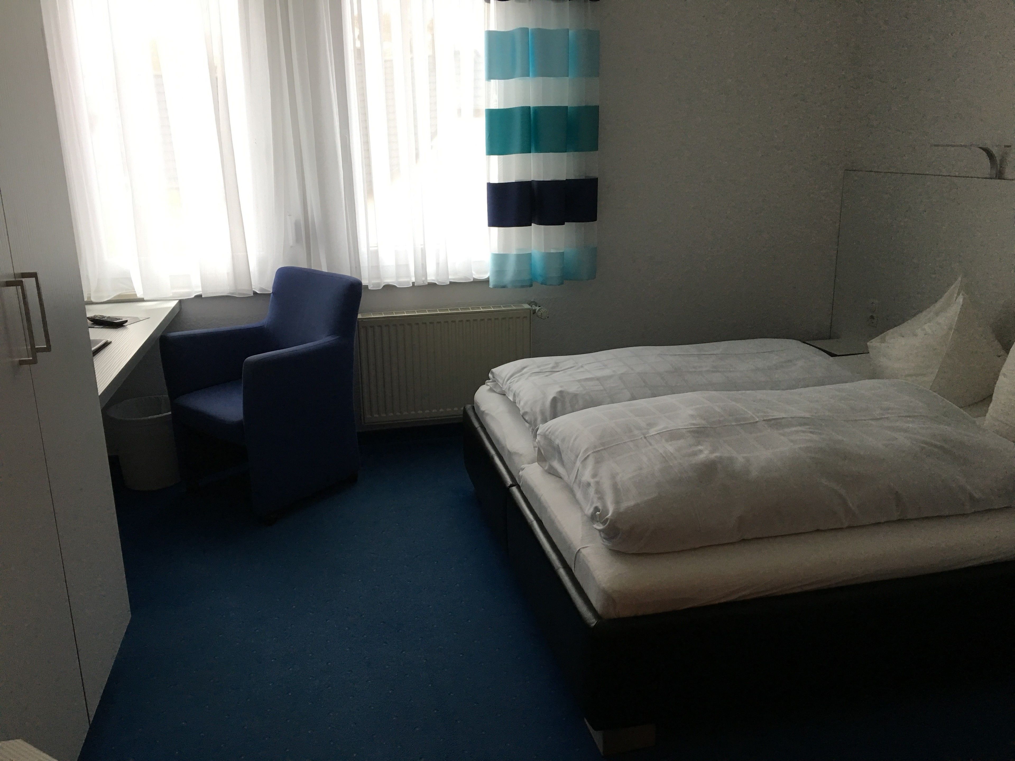 A hotel room with a bed, a desk, a chair, and a window with curtains.