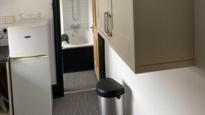 A compact hotel room with a kitchenette, a bathtub, and a trash bin. - Brinkburn Serviced Apartments (Darlington)