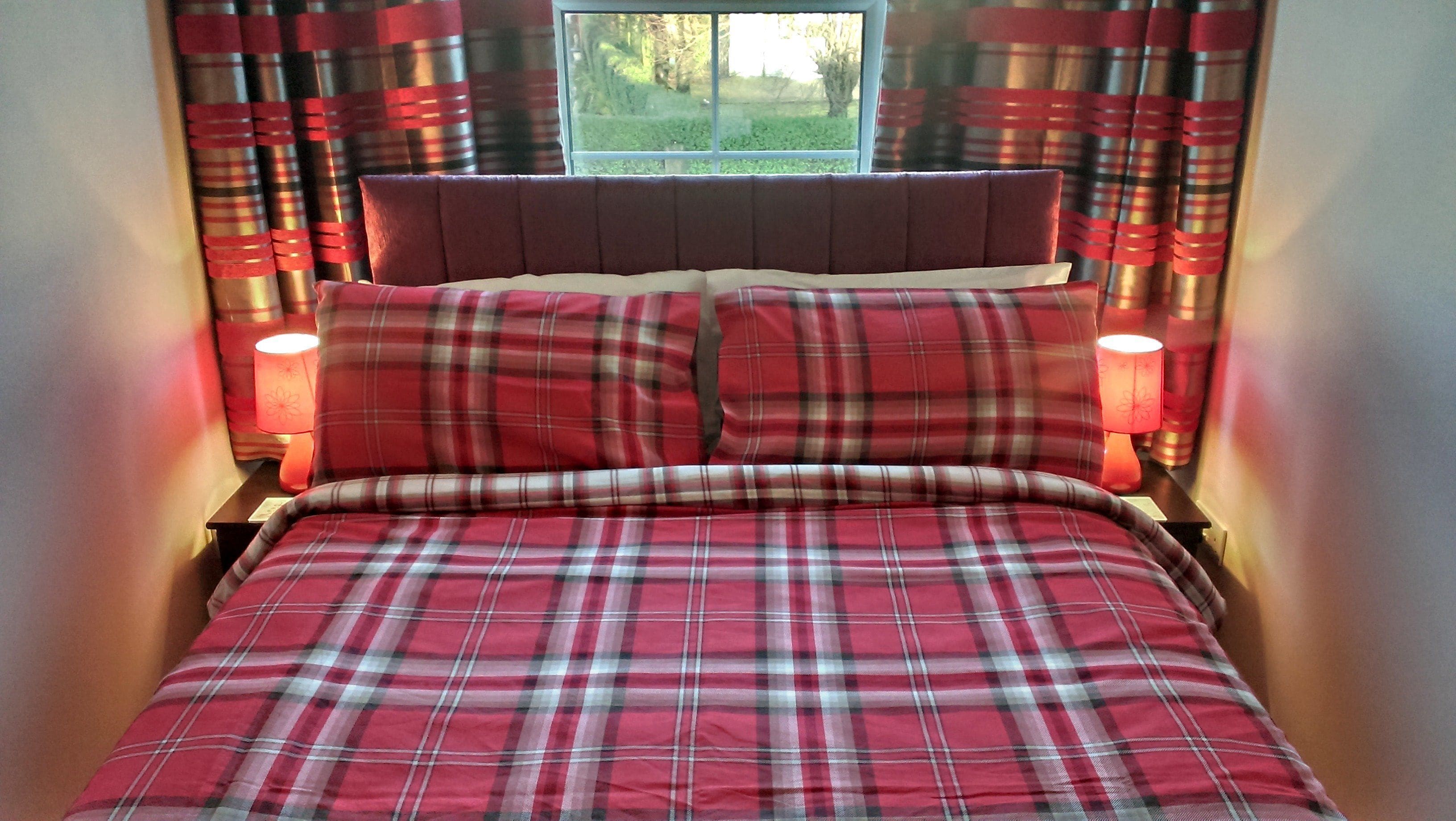 A bed with a red and white plaid bedspread, two matching pillows, and red curtains with a plaid pattern.