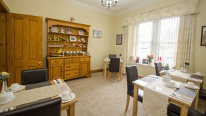 A dining area with a wooden buffet, a laptop on a desk, and a window with curtains.