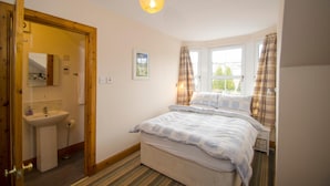 A bedroom with a bed, a window with curtains, a bedside table, and a bathroom with a sink and mirror.