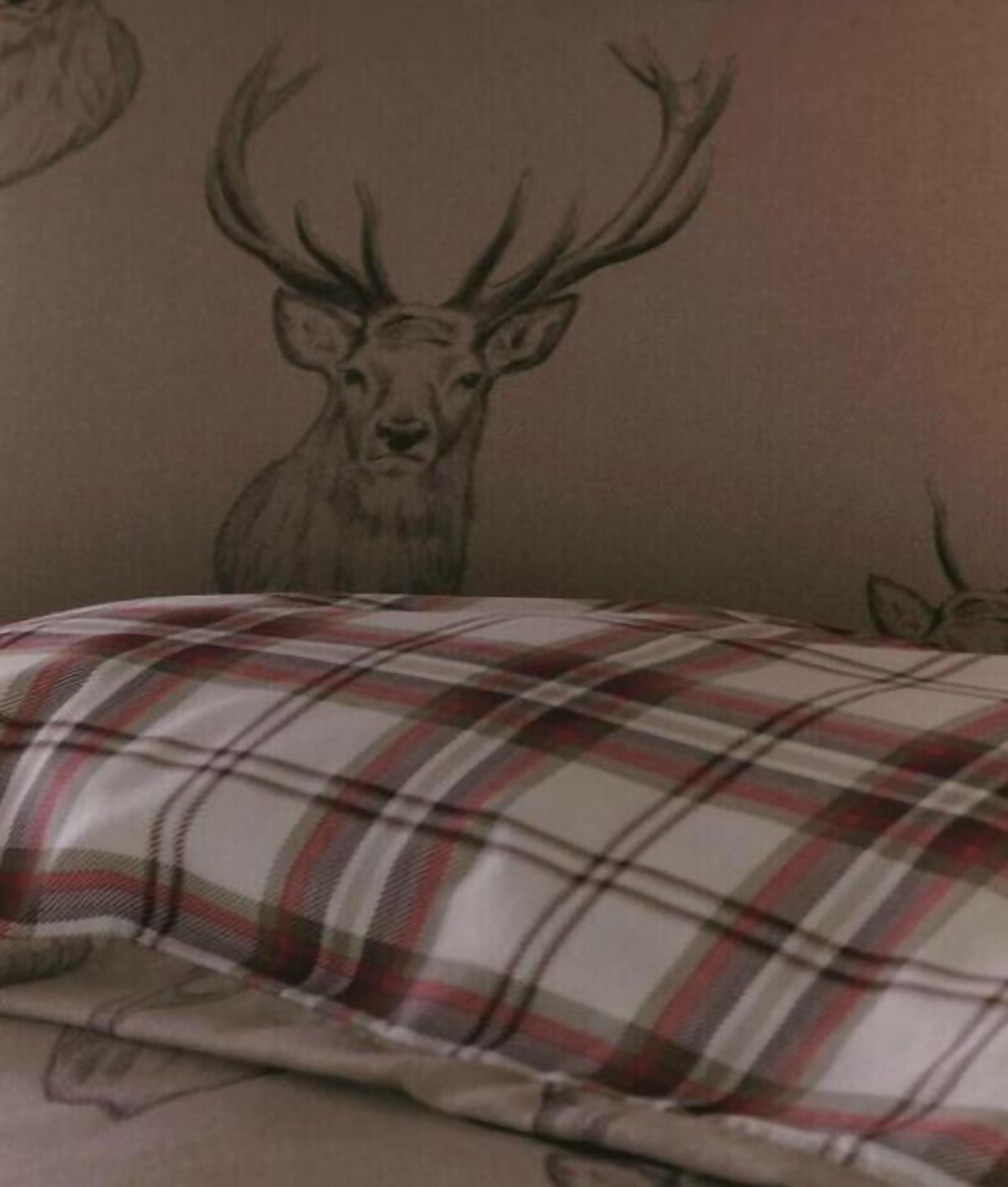 A bed with a plaid blanket and a wall with a deer head design.