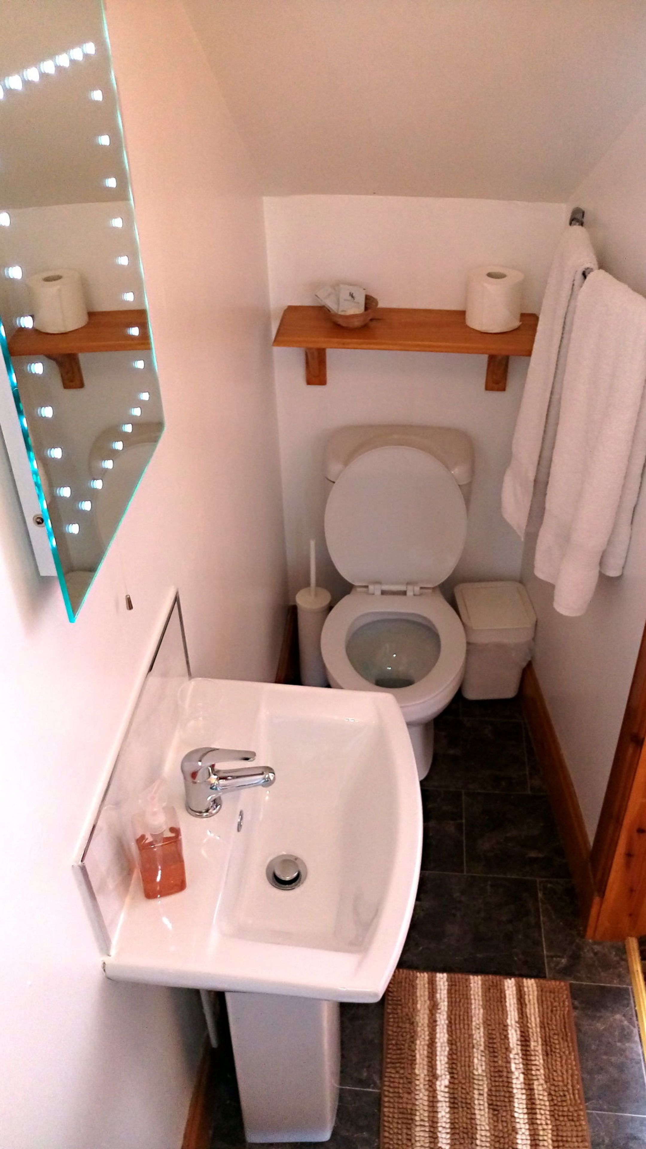 A small bathroom with a white sink, toilet, and a mirror with lights.