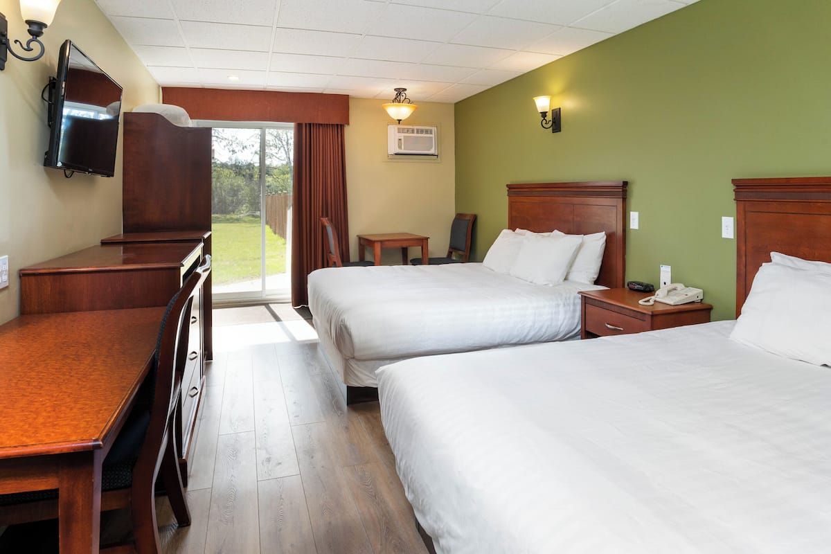 A hotel room with two beds, a desk, a chair, a television, and a small table.