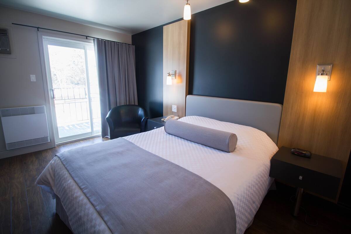 A hotel room with a large bed, a chair, a desk, and a sliding door to a balcony.