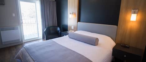 Une chambre d’hôtel avec un grand lit, une chaise, un bureau et une porte coulissante donnant sur un balcon.