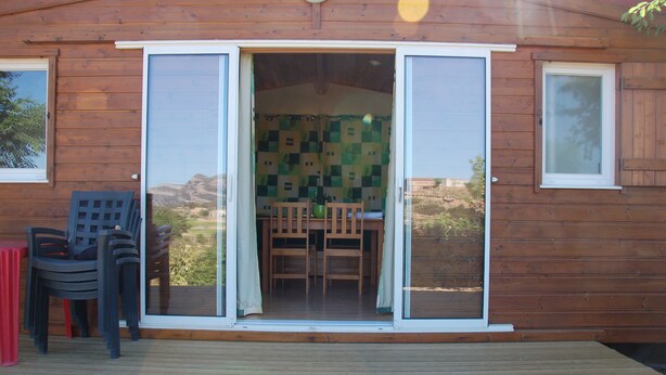 Eine Holzhütte mit einer Schiebetür aus Glas, die auf eine Terrasse mit Tisch und Stühlen führt.
