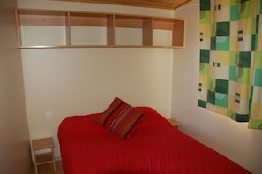 Una habitación con una cama, una mesita de noche de madera y una repisa sobre la cama.