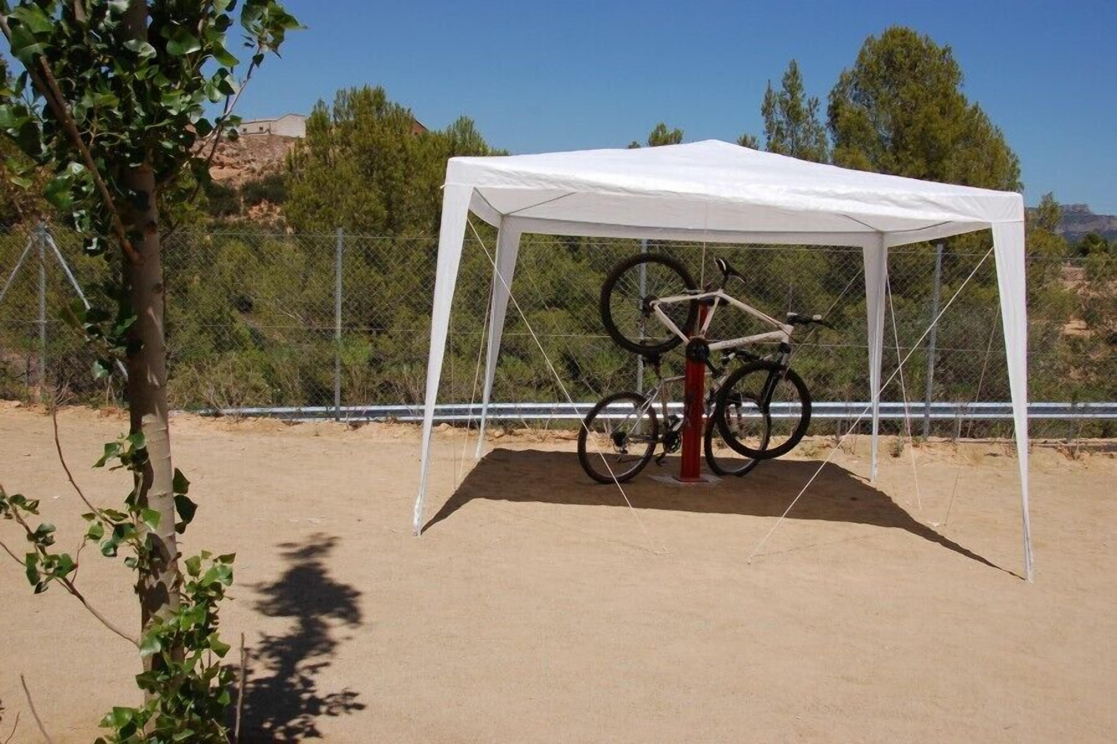 A tent with a bicycle inside, surrounded by a fence and trees.