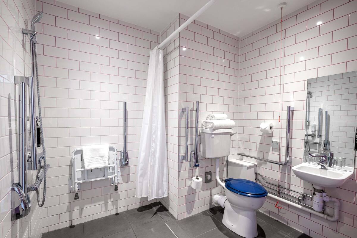 A modern bathroom with white subway tiles, a shower, a toilet with a blue lid, a sink, and a mirror.