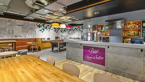 A restaurant with a bar area, wooden tables, and a cityscape mural on the wall. - Ibis Styles Glasgow Centre George Square (Glasgow)