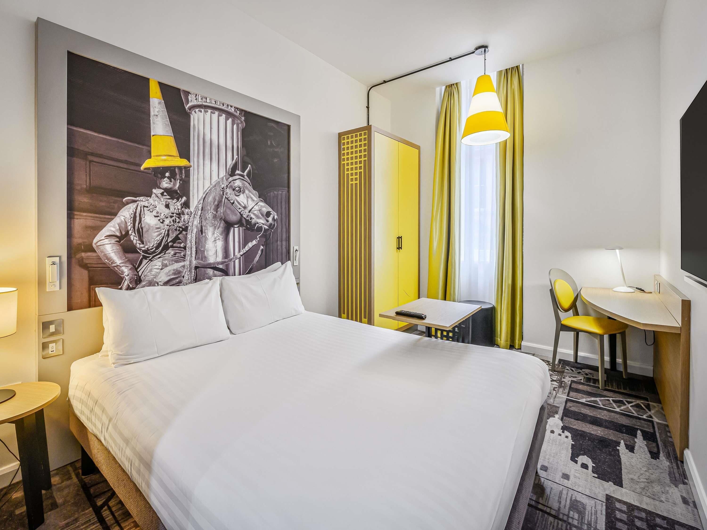 Ein Hotelzimmer mit Bett, Schreibtisch, Stuhl, Lampe und einer großen Wandmalerei.