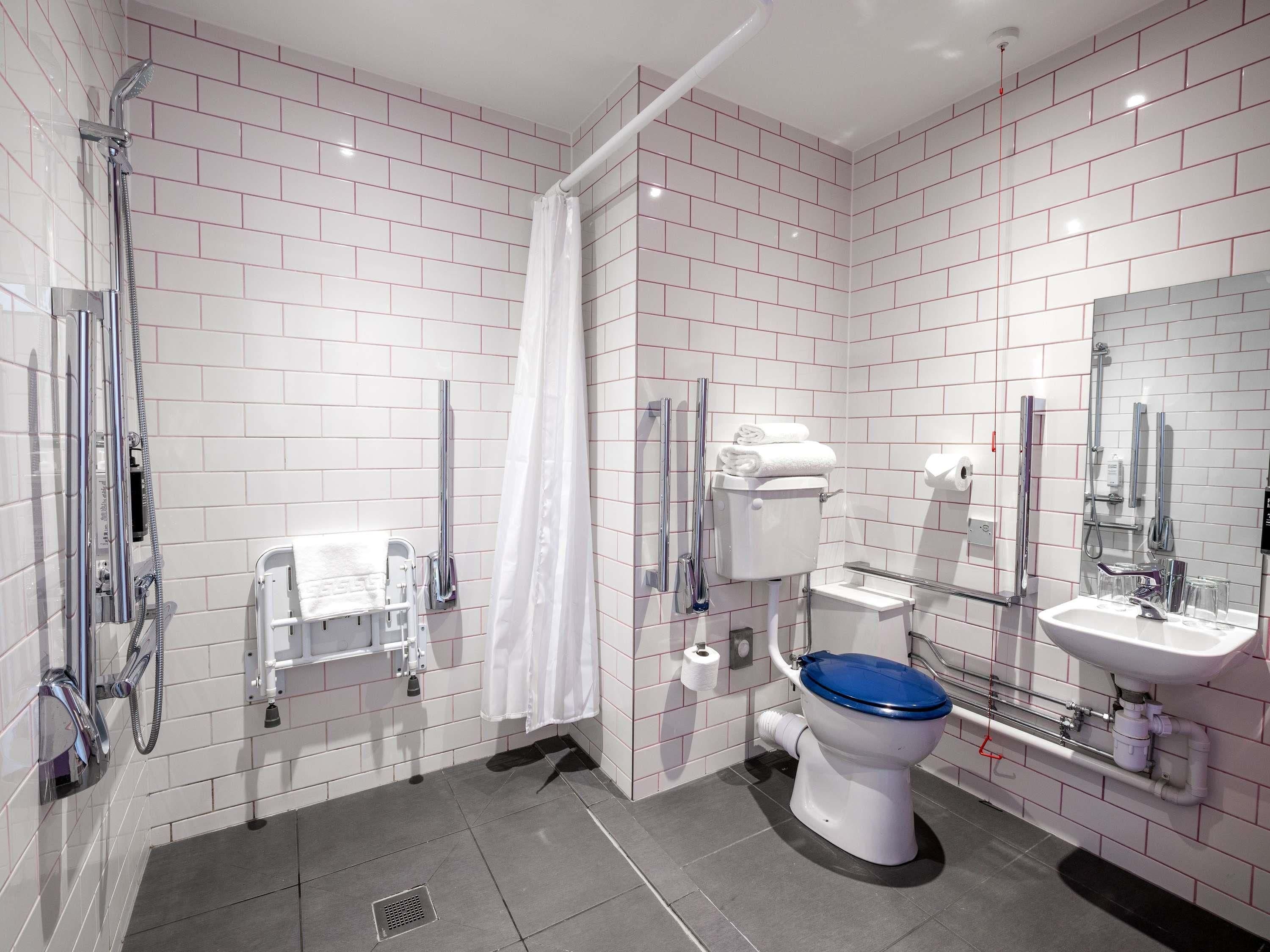 A modern bathroom with white subway tiles, a shower, a toilet with a blue lid, a sink, and a mirror.