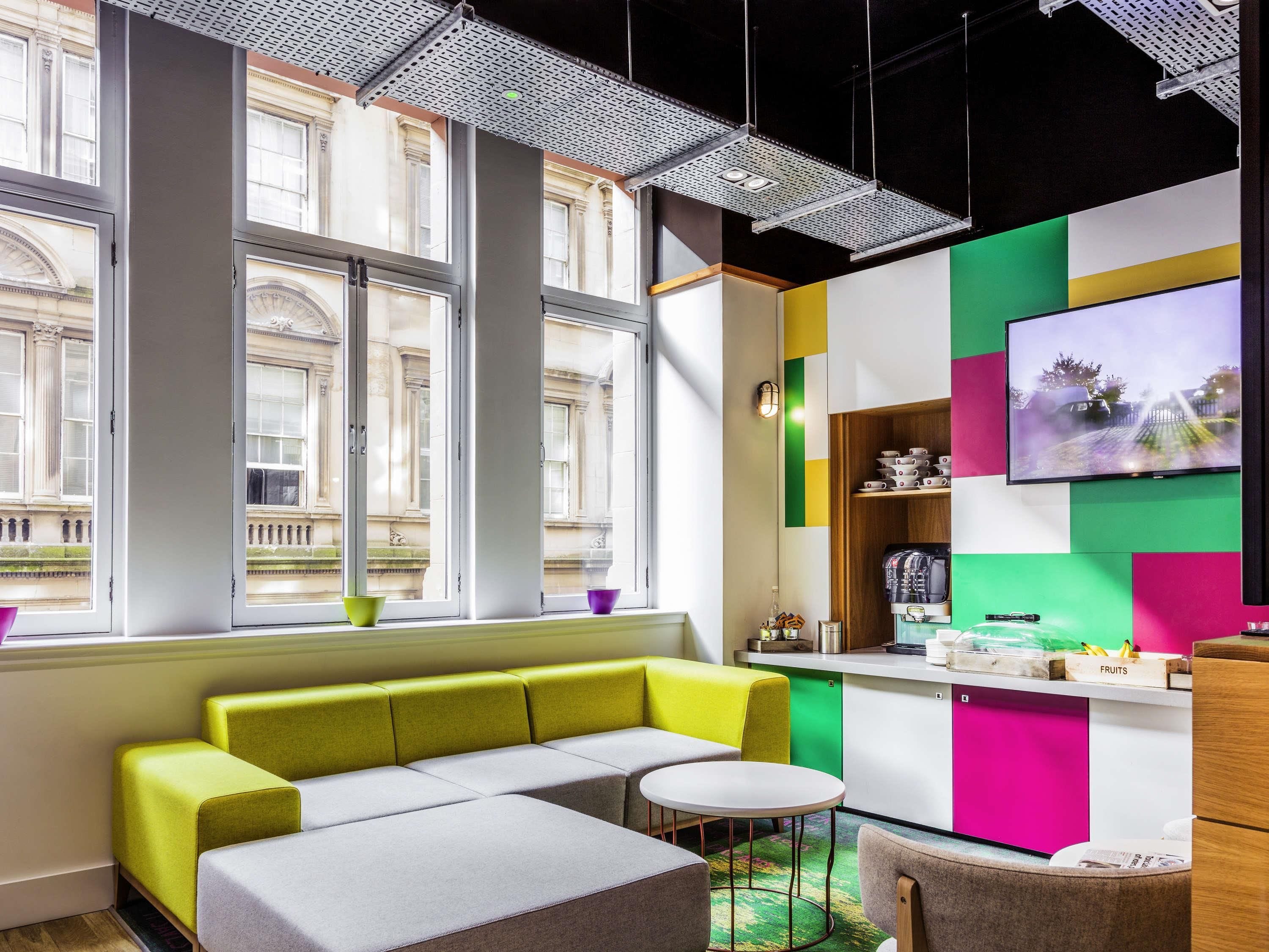 A modern interior with large windows, a sofa, a small table, and a kitchen area.