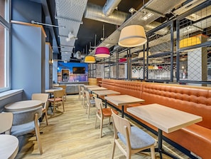 A modern restaurant interior with wooden tables, cushioned booths, and a cityscape mural on the wall.