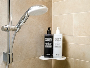A bathroom with a shower, two bottles of hair care products on a shelf, and a tiled wall.